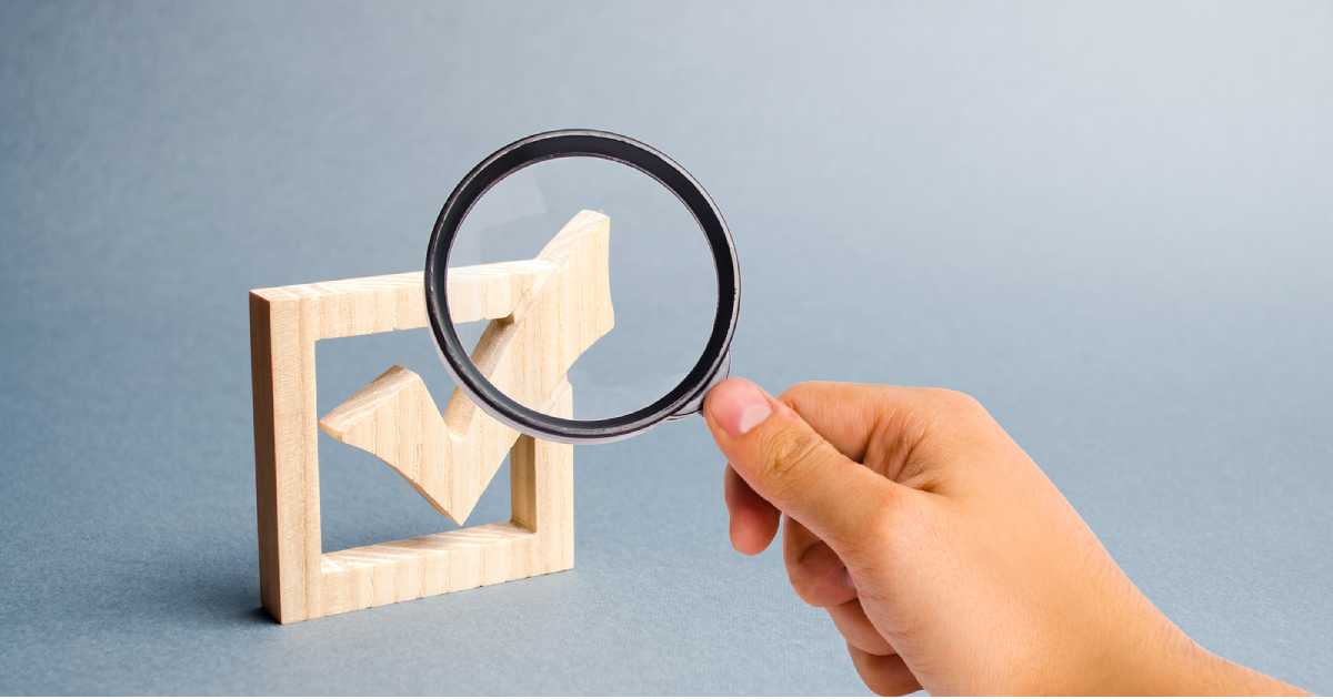 hand holding magnifying glass over wooden checkmark