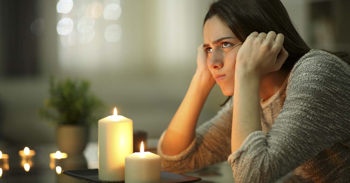 Frustrated woman sitting in the dark using candles during a power outage, illustrating the inconvenience of not having a propane-powered generator in North Texas.